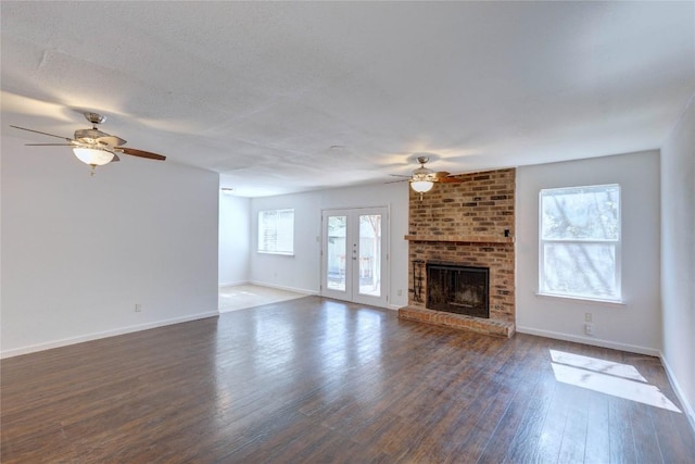 unfurnished living room featuring french doors, dark hardwood / wood-style flooring, a brick fireplace, and ceiling fan