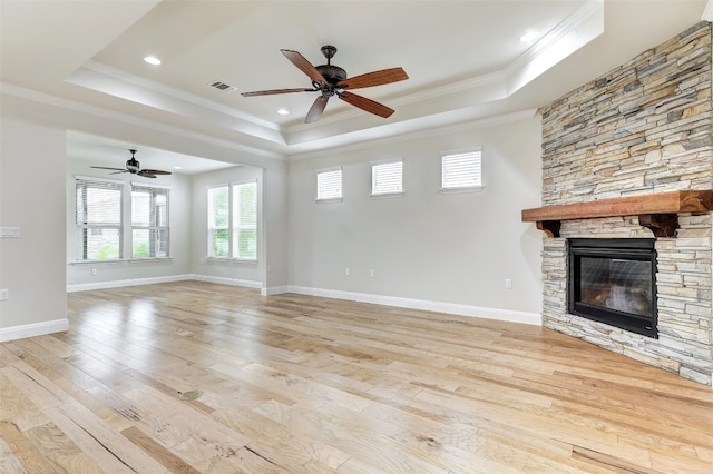 unfurnished living room featuring light hardwood / wood-style flooring, a tray ceiling, ceiling fan, and a stone fireplace