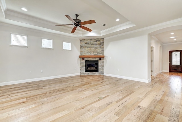 unfurnished living room with ceiling fan, a raised ceiling, a fireplace, light wood-type flooring, and crown molding