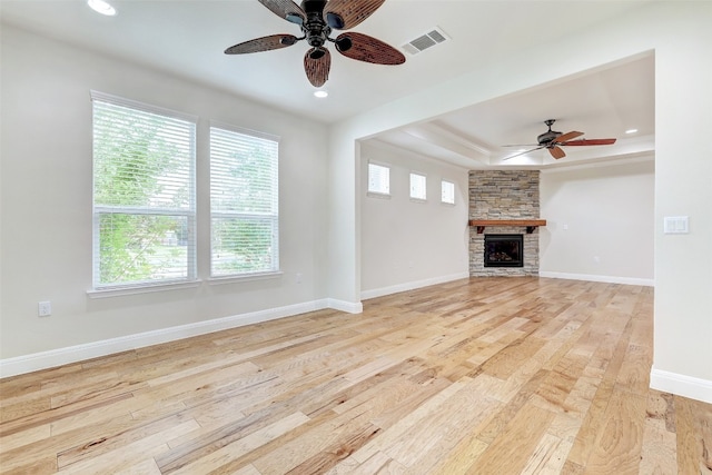 unfurnished living room with ceiling fan, a stone fireplace, light hardwood / wood-style flooring, and plenty of natural light