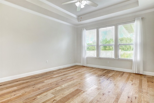 empty room featuring light wood-type flooring, a tray ceiling, ornamental molding, and ceiling fan