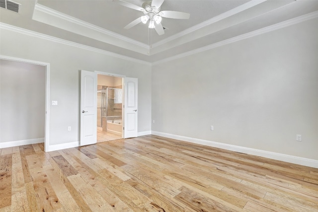 unfurnished bedroom with ceiling fan, connected bathroom, ornamental molding, a tray ceiling, and light hardwood / wood-style floors