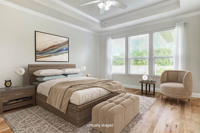 bedroom with light hardwood / wood-style floors, ceiling fan, a raised ceiling, and crown molding