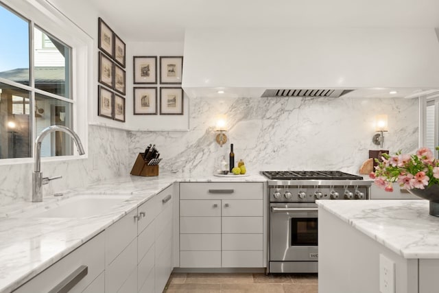 kitchen with light stone counters, white cabinets, sink, backsplash, and stainless steel stove