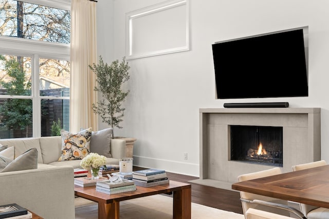 living area featuring baseboards, a fireplace with flush hearth, and wood finished floors