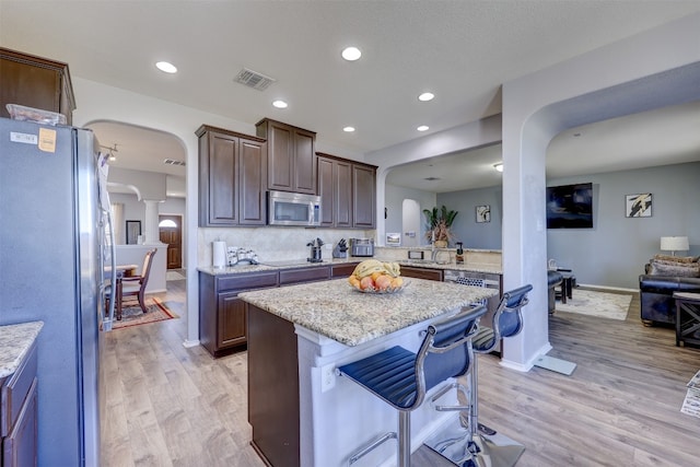 kitchen with a kitchen island, light stone countertops, appliances with stainless steel finishes, light hardwood / wood-style floors, and dark brown cabinetry