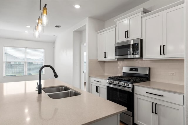 kitchen featuring decorative light fixtures, appliances with stainless steel finishes, white cabinetry, sink, and decorative backsplash