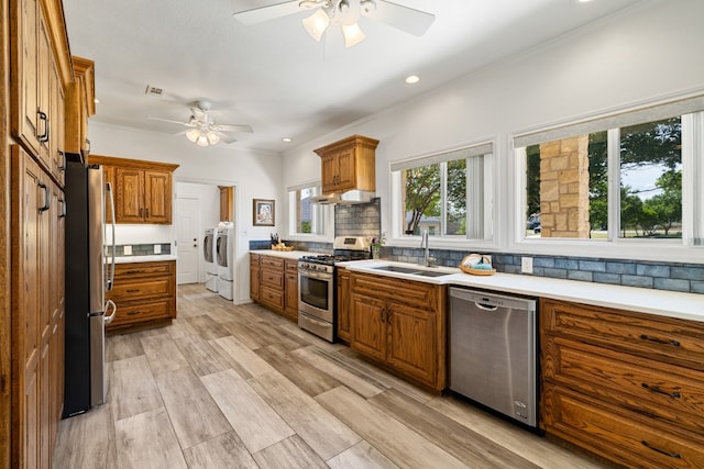 kitchen with light wood-type flooring, sink, washing machine and clothes dryer, stainless steel appliances, and ceiling fan