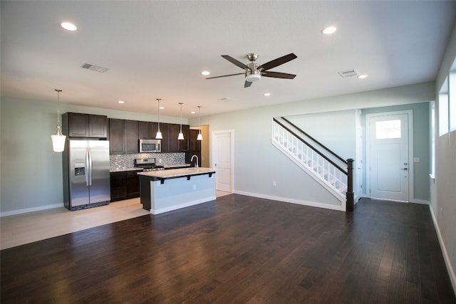 kitchen with a kitchen island with sink, stainless steel appliances, a kitchen breakfast bar, wood-type flooring, and ceiling fan