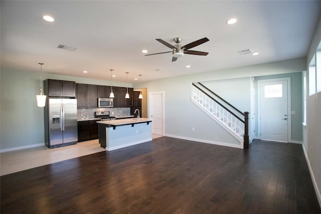 kitchen featuring visible vents, backsplash, a center island with sink, a kitchen bar, and appliances with stainless steel finishes