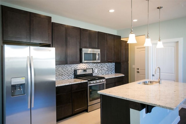 kitchen featuring light stone counters, an island with sink, a sink, appliances with stainless steel finishes, and backsplash