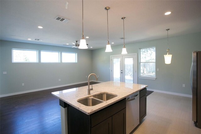 kitchen with a center island with sink, hanging light fixtures, stainless steel appliances, sink, and light stone counters