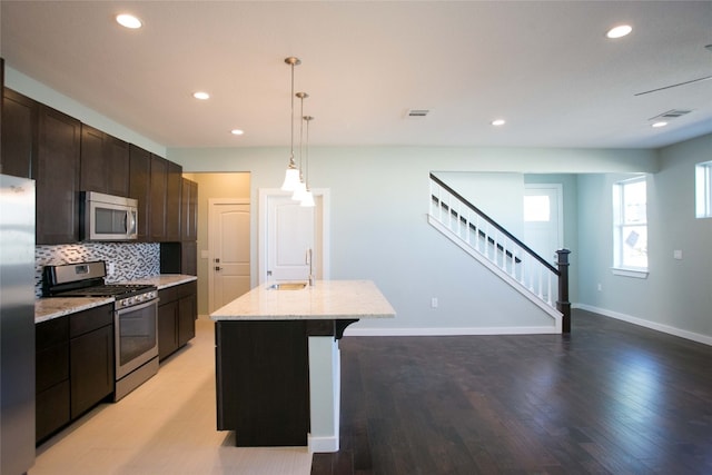 kitchen featuring light hardwood / wood-style flooring, stainless steel appliances, sink, light stone countertops, and an island with sink