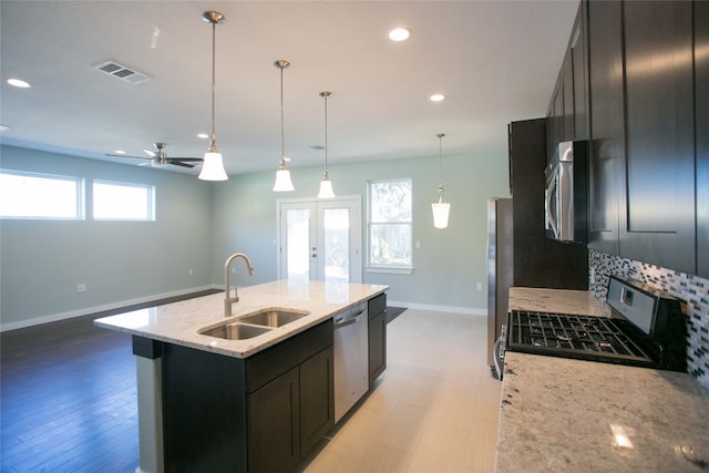 kitchen featuring an island with sink, stainless steel appliances, sink, ceiling fan, and light stone counters