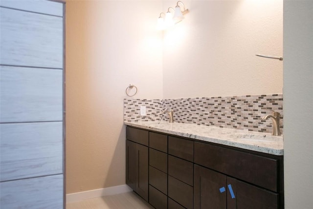 full bathroom featuring a sink, baseboards, tasteful backsplash, and double vanity