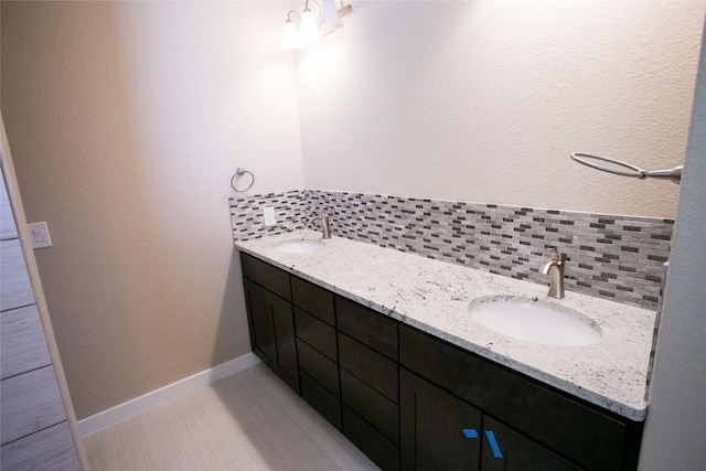 full bath featuring double vanity, baseboards, tasteful backsplash, and a sink