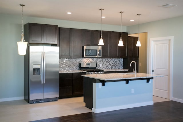 kitchen with a kitchen island with sink, light hardwood / wood-style flooring, stainless steel appliances, sink, and light stone countertops