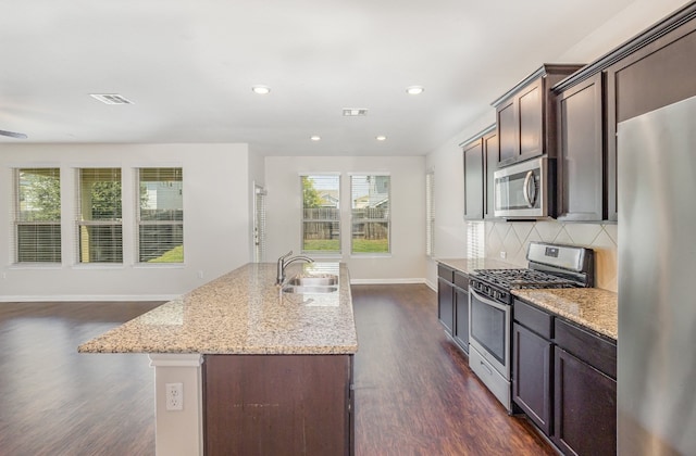 kitchen with light stone countertops, a center island with sink, appliances with stainless steel finishes, dark wood-type flooring, and sink