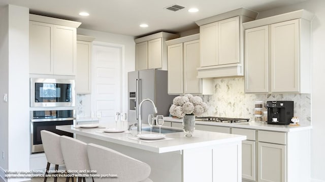 kitchen featuring appliances with stainless steel finishes, backsplash, a kitchen breakfast bar, custom range hood, and a center island with sink