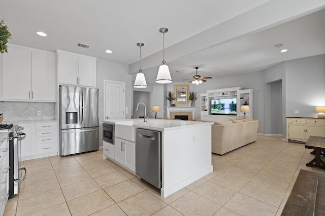 kitchen featuring ceiling fan, pendant lighting, a kitchen island with sink, white cabinets, and appliances with stainless steel finishes