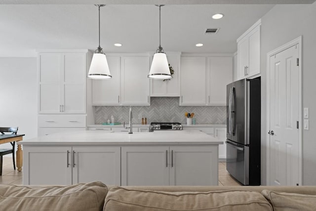 kitchen featuring a center island with sink, white cabinets, appliances with stainless steel finishes, tasteful backsplash, and decorative light fixtures