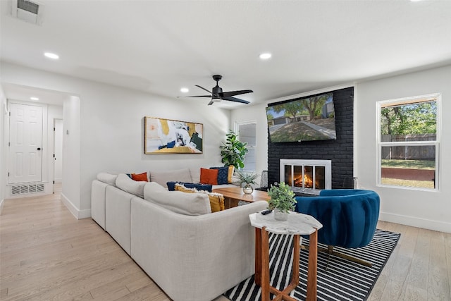 living room featuring a fireplace, light wood-type flooring, and ceiling fan