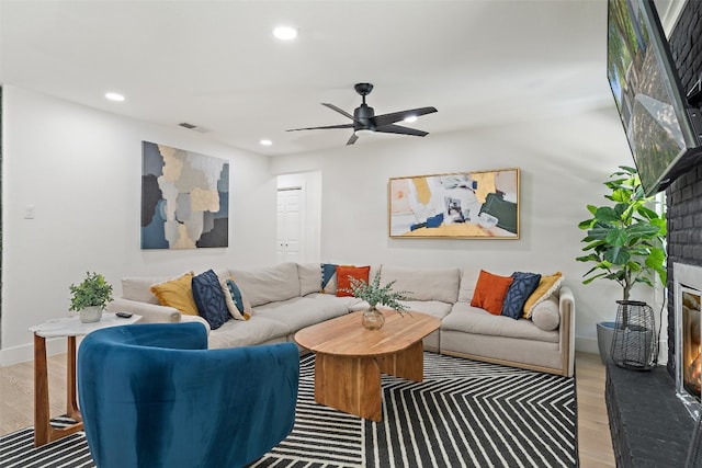 living room with ceiling fan, wood-type flooring, and a fireplace