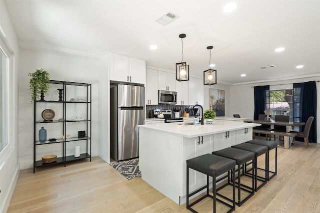 kitchen featuring hanging light fixtures, a center island with sink, stainless steel appliances, and light hardwood / wood-style flooring