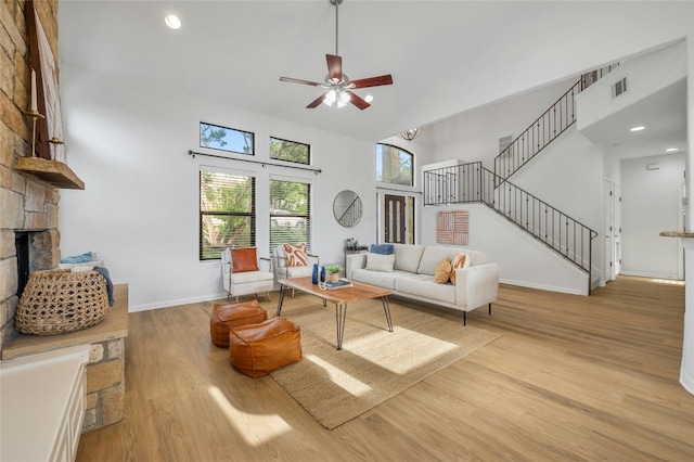 living room featuring light wood-type flooring, a high ceiling, ceiling fan, and a stone fireplace