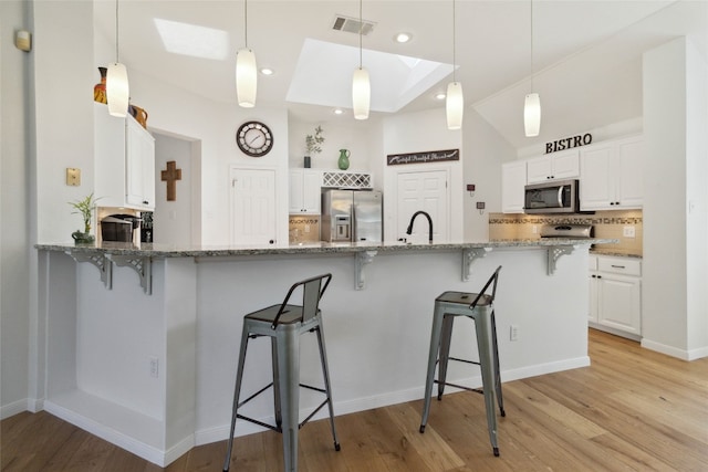 kitchen featuring white cabinets, light stone countertops, stainless steel appliances, and light hardwood / wood-style flooring