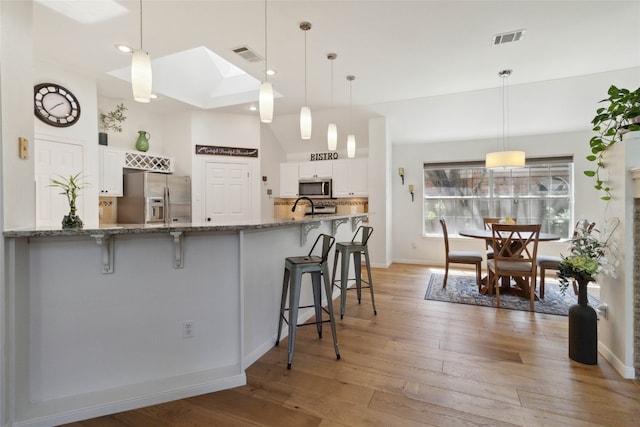 kitchen featuring decorative light fixtures, white cabinets, appliances with stainless steel finishes, and a breakfast bar area