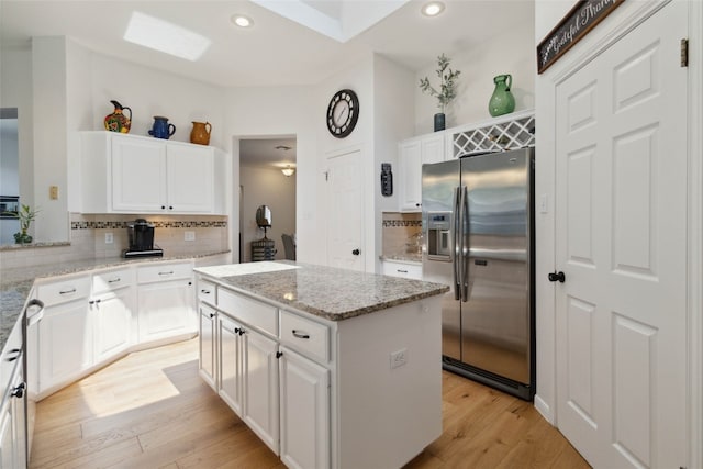 kitchen featuring stainless steel fridge, a center island, light stone countertops, white cabinets, and light hardwood / wood-style floors