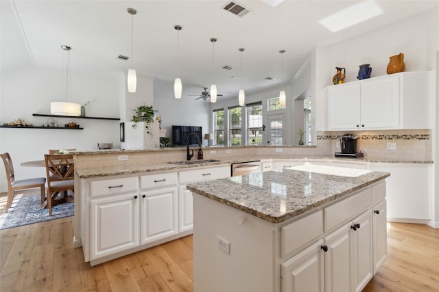 kitchen featuring light hardwood / wood-style flooring, kitchen peninsula, a center island, light stone countertops, and hanging light fixtures