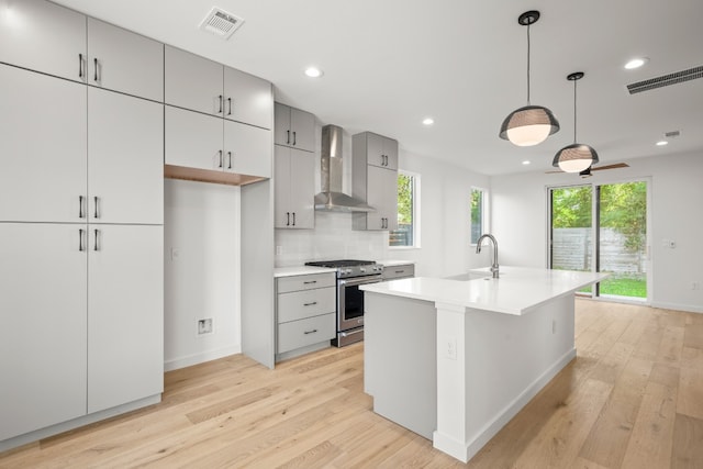 kitchen featuring light wood-type flooring, a healthy amount of sunlight, stainless steel range with gas cooktop, and wall chimney range hood