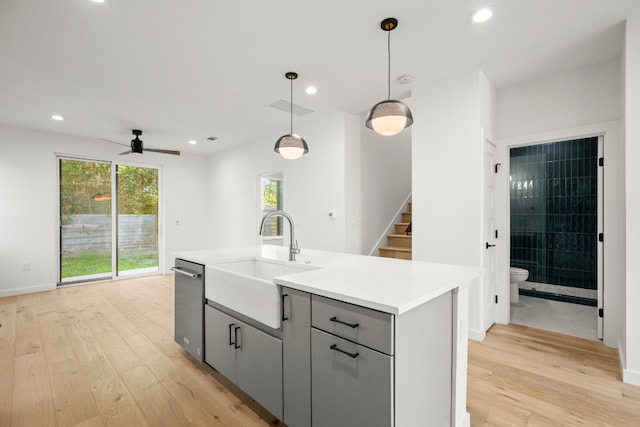 kitchen featuring gray cabinetry, a center island with sink, light hardwood / wood-style floors, stainless steel dishwasher, and sink