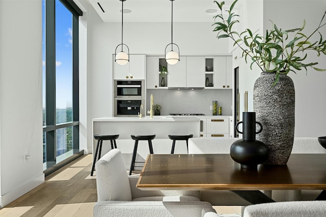 kitchen featuring decorative light fixtures, white cabinetry, double oven, and light hardwood / wood-style flooring