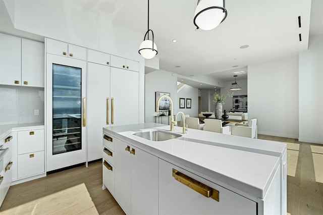 kitchen featuring white cabinetry, sink, pendant lighting, a kitchen island with sink, and light wood-type flooring