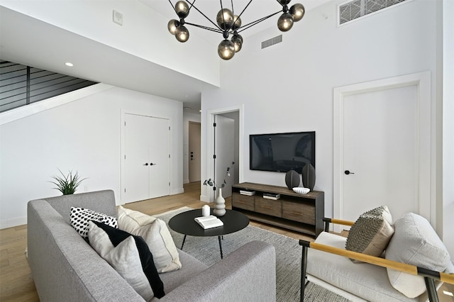 living room with a towering ceiling, light hardwood / wood-style flooring, and a notable chandelier