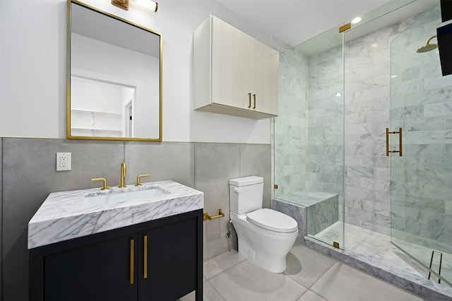 bathroom with tile patterned floors, toilet, vanity, a shower with shower door, and tile walls