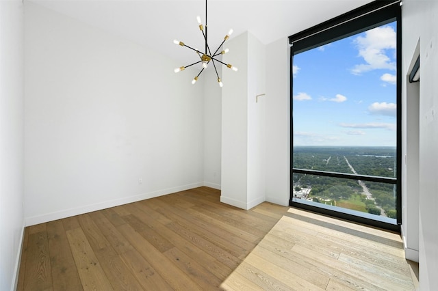 unfurnished room featuring floor to ceiling windows, a wealth of natural light, light hardwood / wood-style flooring, and an inviting chandelier