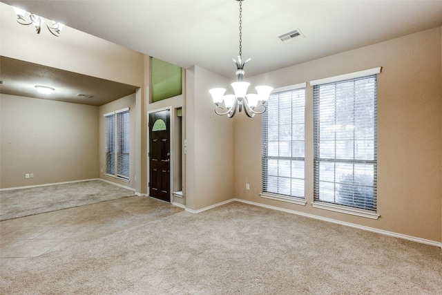 empty room with light colored carpet and a notable chandelier