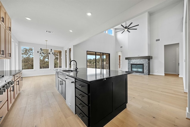 kitchen featuring light brown cabinets, dishwasher, a tile fireplace, pendant lighting, and a kitchen island with sink