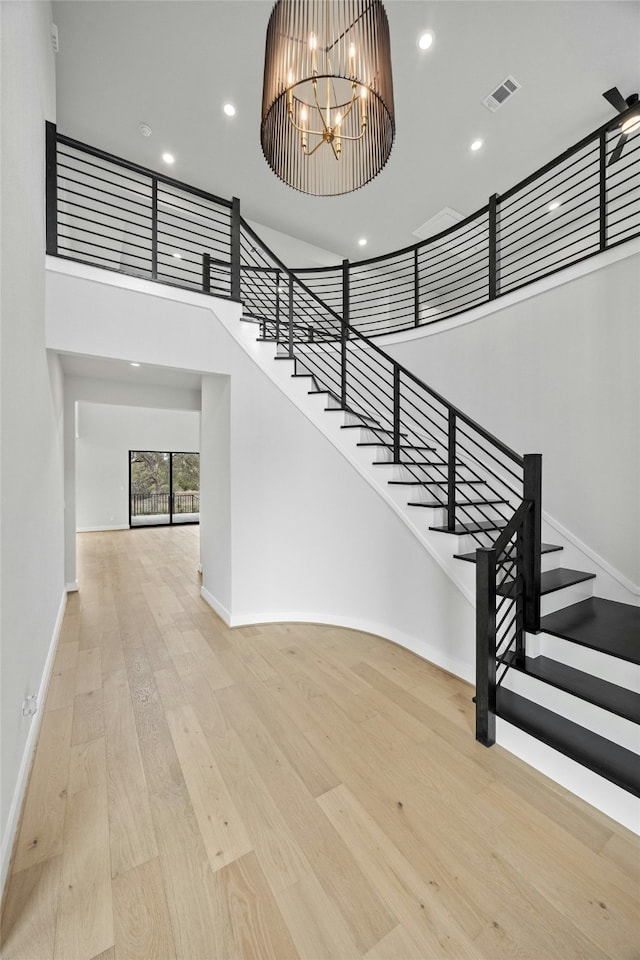 staircase with wood-type flooring, a towering ceiling, and a notable chandelier