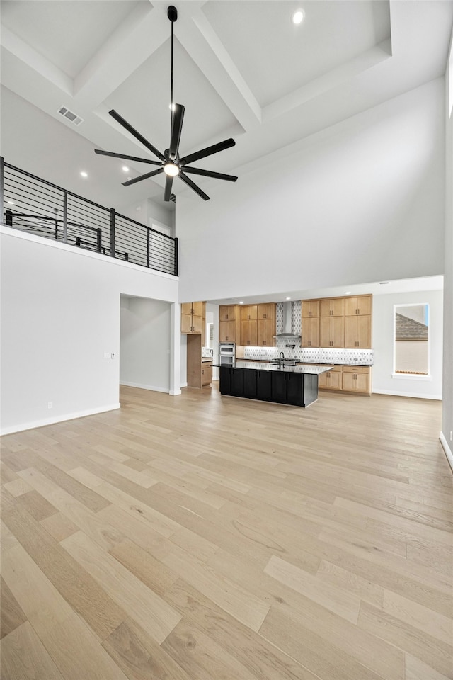 unfurnished living room featuring ceiling fan, sink, light wood-type flooring, and a towering ceiling