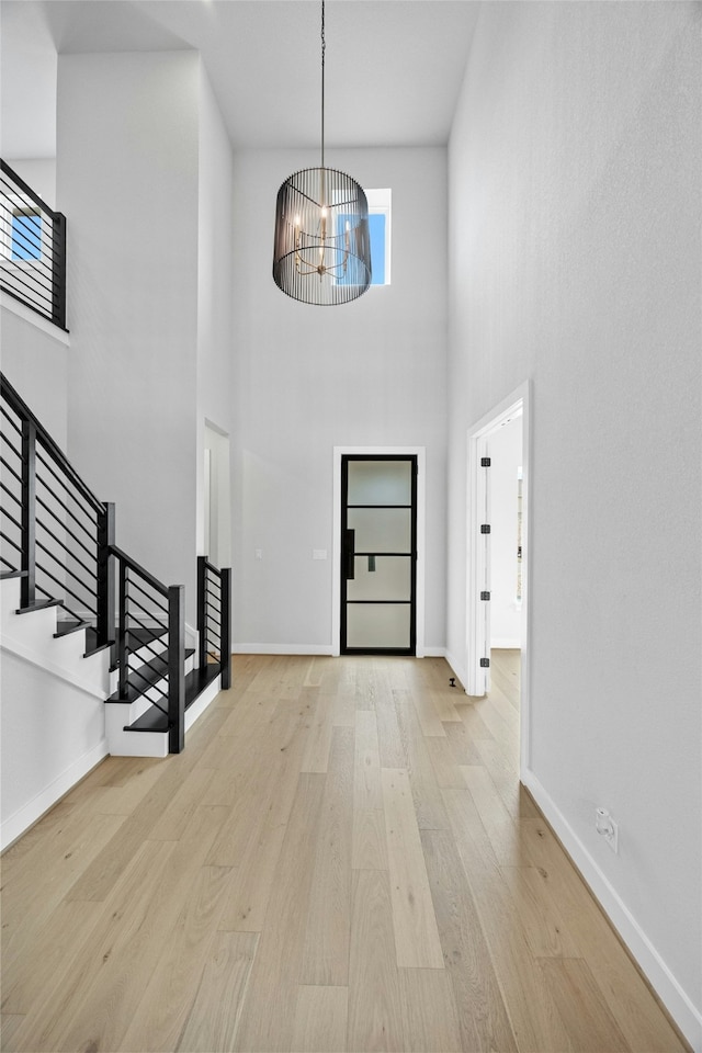 foyer entrance featuring a notable chandelier, light hardwood / wood-style flooring, and a high ceiling