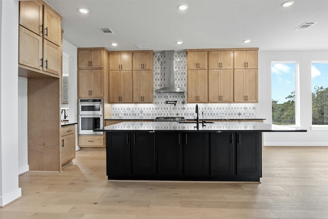 kitchen featuring sink, light hardwood / wood-style floors, wall chimney exhaust hood, and a center island with sink