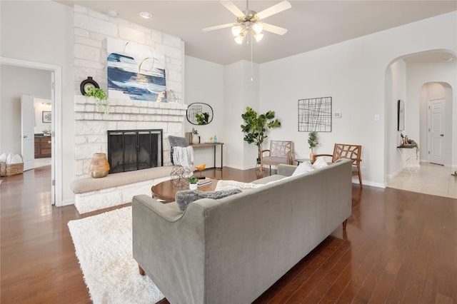 living room with ceiling fan, dark wood-type flooring, and a stone fireplace