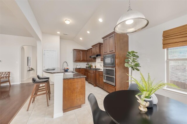 kitchen with pendant lighting, dark stone countertops, light tile patterned floors, an island with sink, and appliances with stainless steel finishes