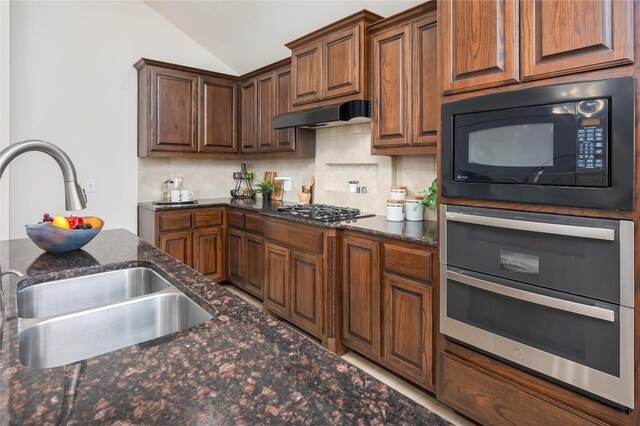 kitchen with appliances with stainless steel finishes, dark stone counters, lofted ceiling, and sink