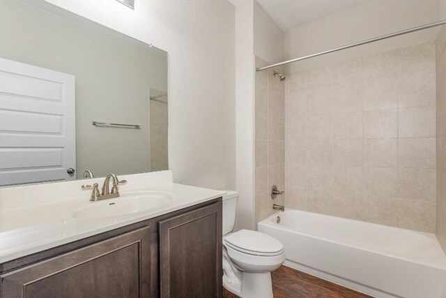 full bathroom featuring hardwood / wood-style floors, tiled shower / bath, toilet, and vanity